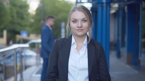 Beautiful Young Businesswoman Posing at Business Center Entrance with Blurred People at the