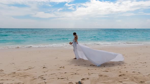 Bride in a White Dress with a Train Stands on the Tropical Beach, Honeymoon on the Seashore. Slow