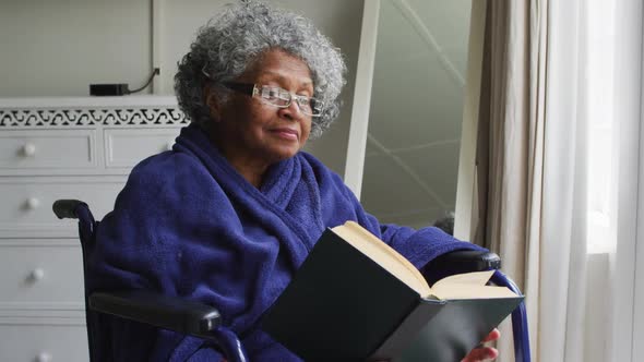 Senior african american woman sitting on the wheelchair reading a book at home