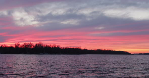 Trees silhouettes during red sunset on the river. The sun in spindrift clouds Fantastic natural