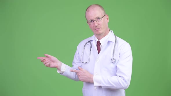 Happy Mature Bald Man Doctor Showing Something Against Green Background