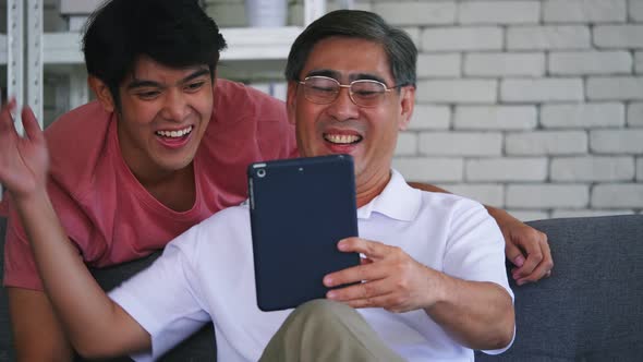 Son and senior father using digital tablet on sofa. Happy family spending time together at home.