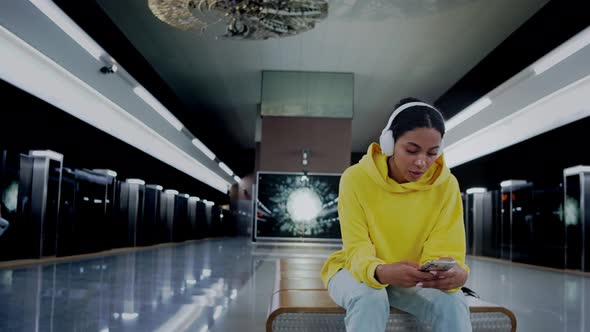 Girl Sitting Waiting for a Train Listening Music in Headphones Clapping Hands