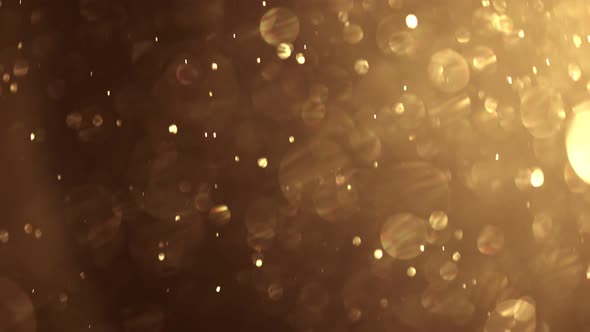 Gold Dust Particles Fly in the Air. Glimmering Glowing Gold Bokeh Background.