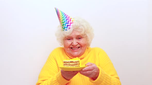 Older Woman with a Gift Wear Yellow Sweater and Horn Cap on a White Background Holding Plate with