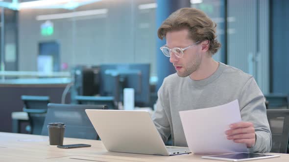 Young Businessman with Laptop Celebrating Success on Documents