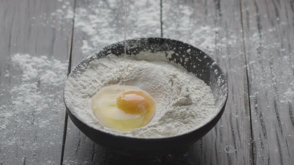 Slowly falling broken egg into a vintage wooden bowl with flour. Cooking dough.