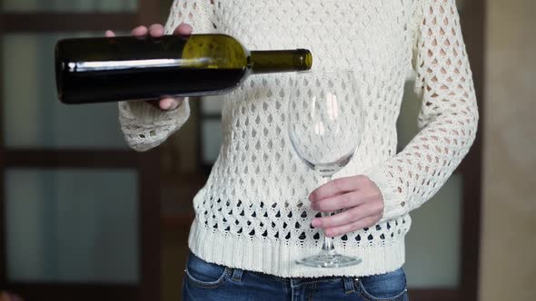 girl pours wine into a glass in the kitchen and drinks. Close-up