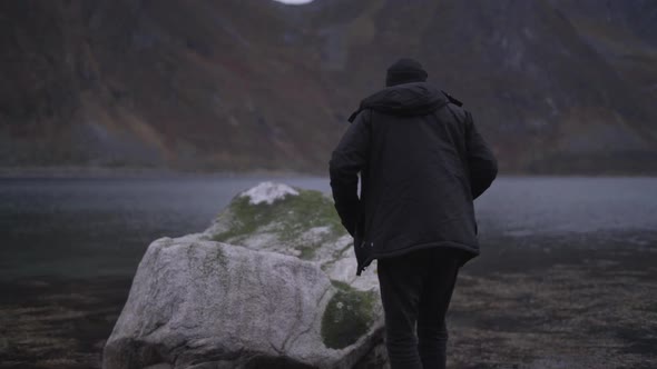 Man Stepping Over Stones To Stand On Fjord Rock