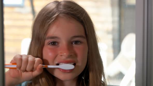 Closeup of the Beautiful Tanned Girl Brushing Her Teeth Looking at the Camera