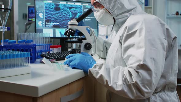 Scientist in Protection Suit Looking Through a Microscope