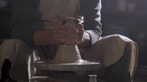 The Potter's Male Hands Shape and Sculpt the Soft White Clay Pot Spinning on a Potter's Wheel in a