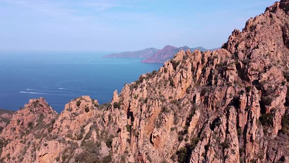 Drone shot of the red rock mountains. Zoom in shot moving past the mountains to the open sea.