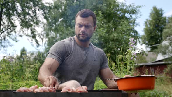 Man is Grilling Meat at Nature Putting Skewers on Barbecue