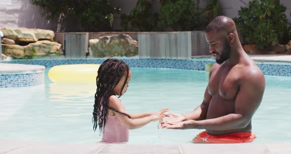 Happy african american father and daughter having fun in swimming pool, clapping hands