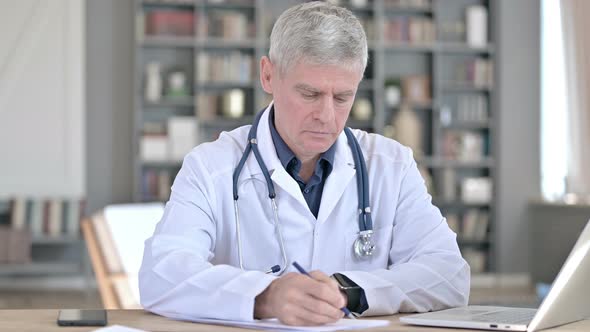 Professional Senior Doctor Writing on Papers While Sitting in Office