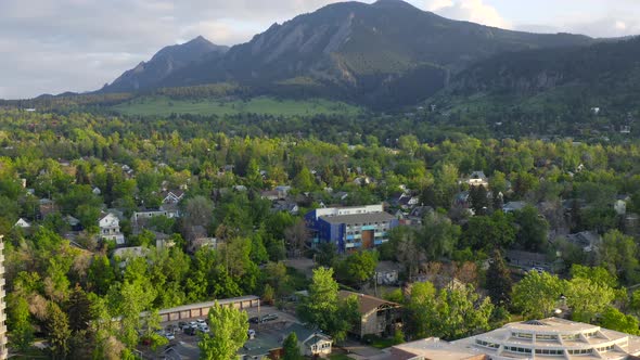 Aerial pan up reveal of beautiful flatiron mountain vista and bright green trees in Boulder Colorado