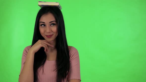 Young Attractive Asian Woman Smiles To Camera with Book on Head - Green Screen Studio