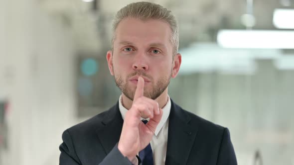 Portrait of Serious Businessman Putting Finger on Lips 