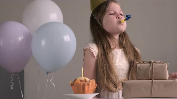 Cute Little Girl Blows Birthday Pipe with Coneshaped Cap on Her Head