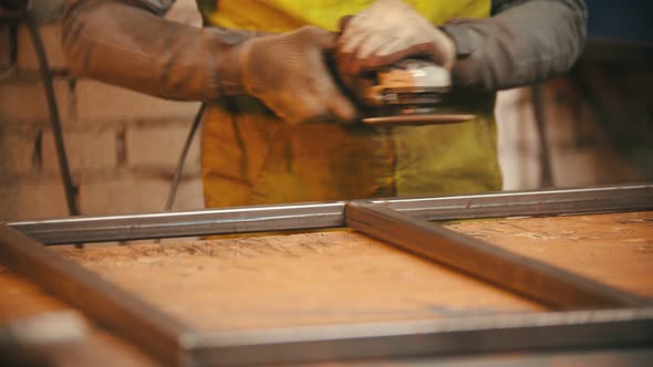 Man Worker Grinding the Seams of an Iron Frame