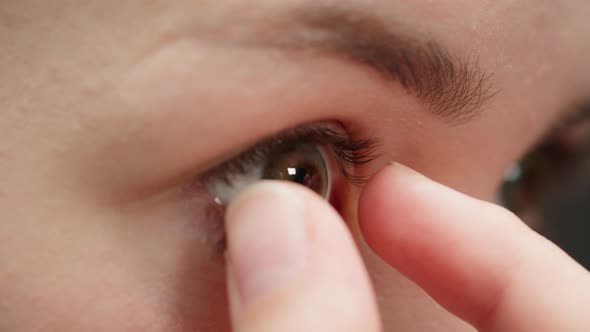 Closeup of a Browneyed Young Woman Taking Off the Decorative Lens with Fingers