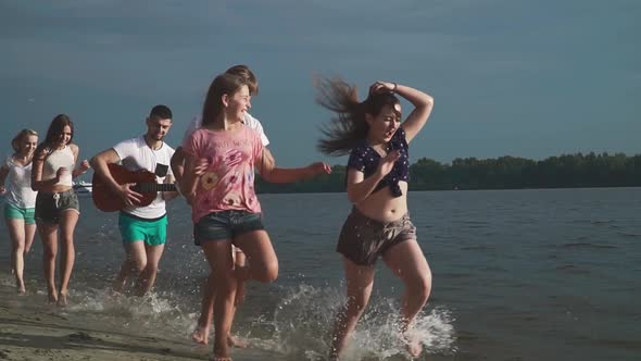 Teenagers Happily Run Along the River Bank