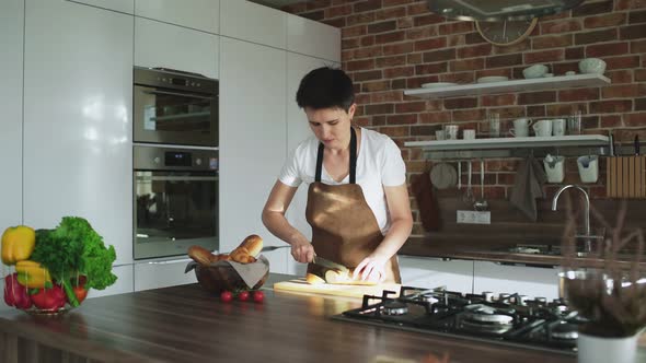 Woman Preparing Breakfast, Cutting Baguette On a Board In the Kitchen