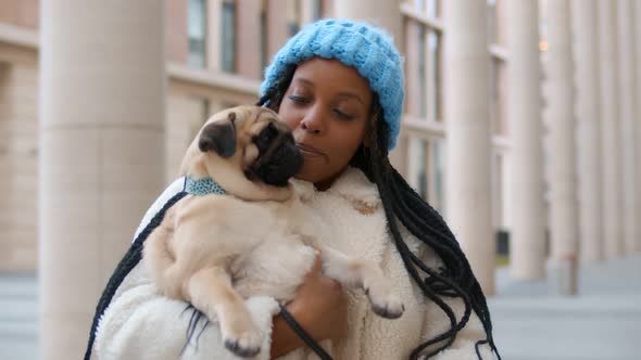 Young African Woman in Warm Clothes Holding Pug Dog Outdoors