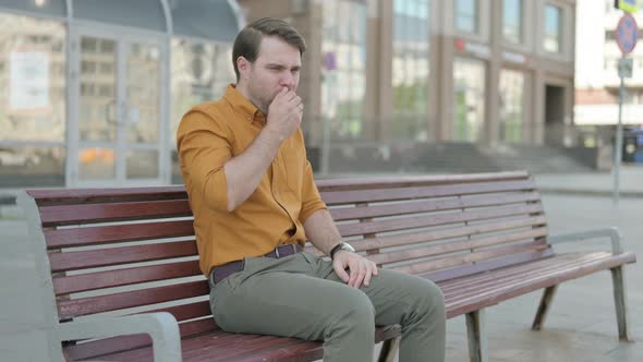 Young Man Coughing while Sitting on Bench Outdoor