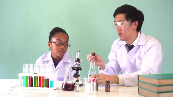 Young Scientist Holding a Flask and Teaching African American Mixed Kid in Chemistry Lab Experiment