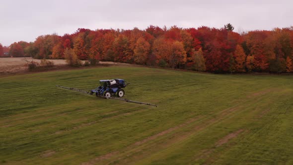 4K Aerial Drone wide shot of tractor sprinkler watering a grass field in Quebec, Canada.