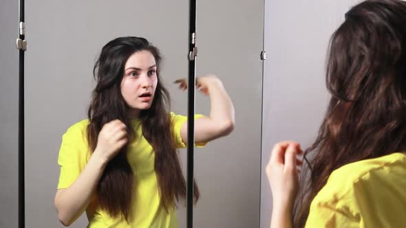 A Woman with Long Hair Stands in Front of a Mirror and Looks at Her Hair Reflection
