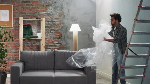 Bearded Black Man Takes Off Plastic From Sofa in Living Room