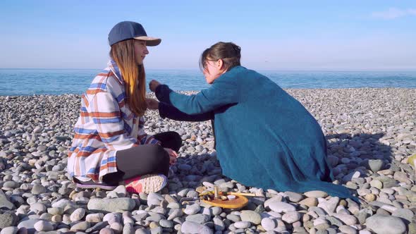 Two women are sitting on the seashore and preparing for a rape ceremony.