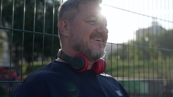 Cheerful Caucasian Greyhaired Mature Man Talking Putting on Headphones in Slow Motion Standing in