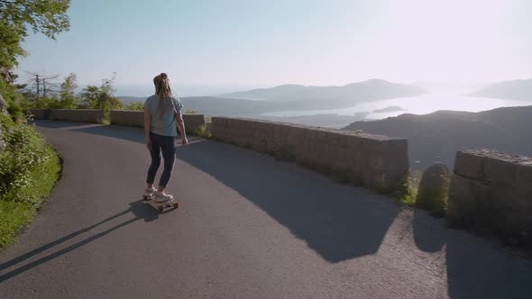 Camera following dreadlocks woman longboarding on mountain background riding skateboard cruising