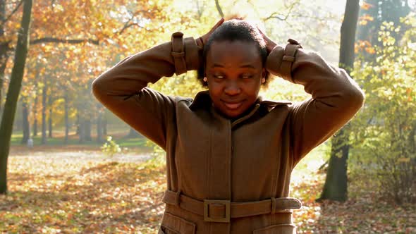 A Young Beautiful African Girl Stands in the Woods and Gives Her Loose Hair Into a Ponytail