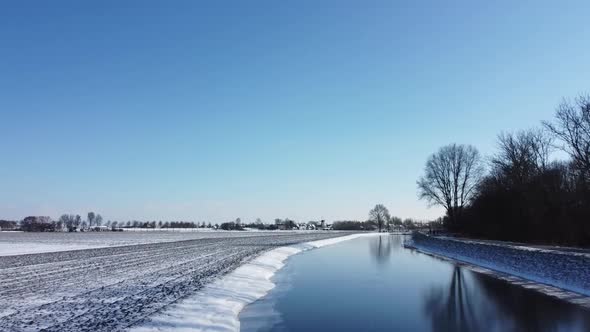 Drone flies over a ditch in a Dutch winter landscape. Reflection in the frozen ditch