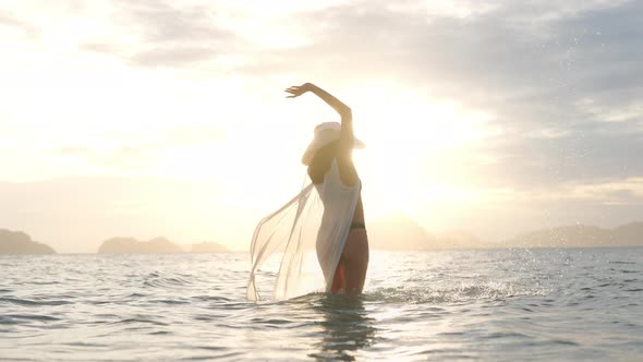 Woman In Thong Splashing Water In Sea Towards Glowing Sunset