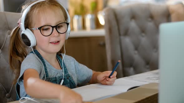 Little Girl is Learning Remotely at Table with Computer at Apartment Room Rbbro