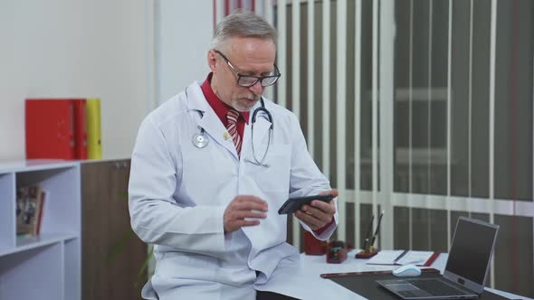 Happy satisfied mature doctor is working with patient via phone.