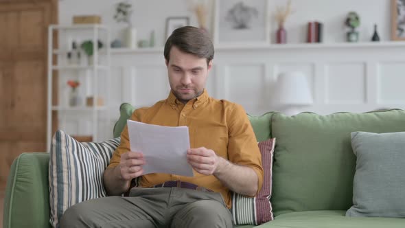 Young Man Celebrating Success on Document on Sofa