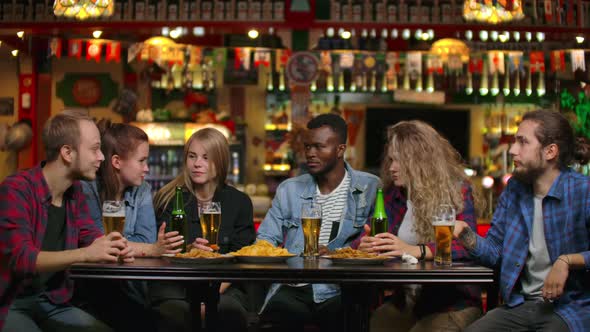 Multiethnic Group of Young Men and Women Drinking Beer at a Bar and Having a Fun Discussion About