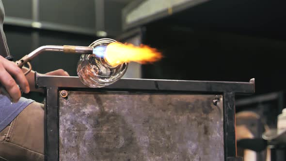 Glass artist torching a spinning vase. Static, low angle