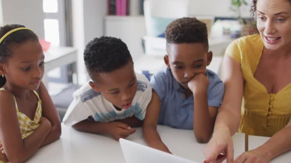 Video of happy caucasian female teacher and african american pupils using laptop