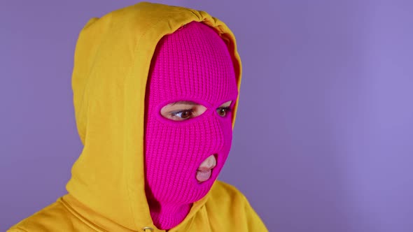 Close Up of Young Woman in Pink Balaclava and Yellow Hood Pondering About Her Life on Purple
