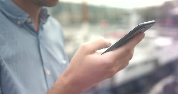 Handsome Caucasian Man Smiles While Using Cell Phone As He Leans Against Railing at End of