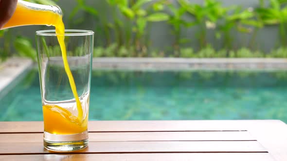Man Hand Pouring Fresh Orange Juice From Bottle in Glass in Tropical Garden