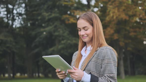 A Young Girl Walks with a Tablet in the Park